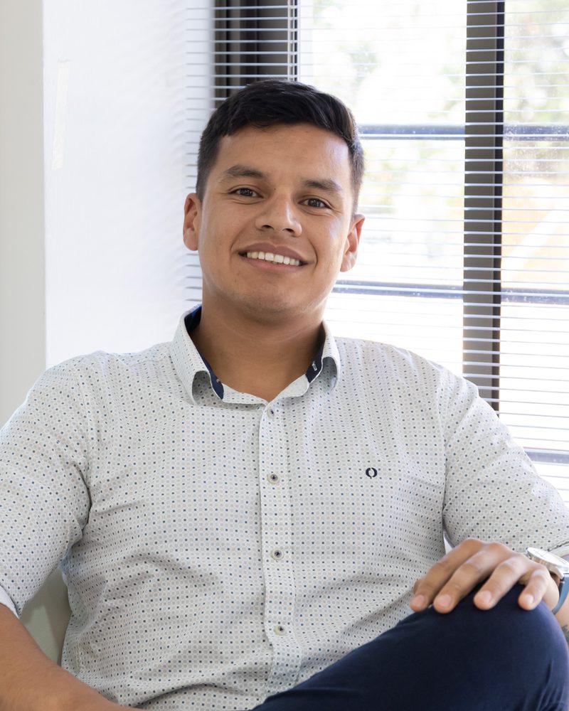 Luis Cortés L., sentado junto a una ventana, sonriendo